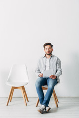 Employee with resume and smartphone looking at camera on chair in office