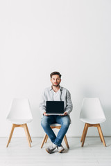 Employee looking at camera while holding laptop with blank screen in office
