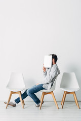Fototapeta premium Side view of employee covering face with laptop while sitting on chair
