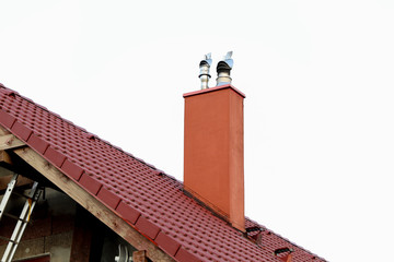 Detail of a chimney on a red classic saddle tile roof separated on a white background. Chimney with two steel pipes. Roof and chimney of family house.