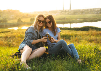 Two cheerful girls and young friends with sunglasses, drinking beer and enjoying the time spent together at sunset.