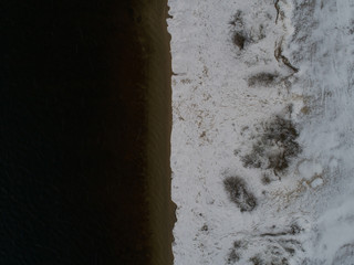 Top down aerial of river coast with white snow, dark water and blue ice
