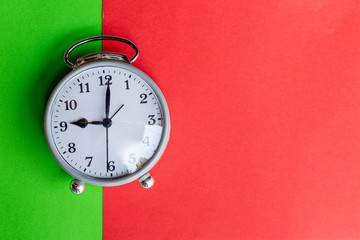 Gray alarm clock on green and red paper background.