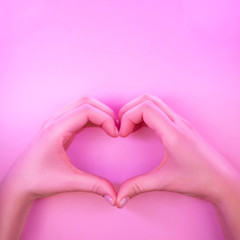 Young woman's hands made gesture of heart shape in trendy neon light on pink background. Love concept.