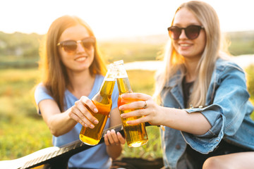 Two cheerful girls and young friends with sunglasses, drinking beer and enjoying the time spent together at sunset.
