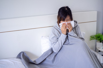 Sick woman was blowing the nose sitting under the blanket. Fever with seasonal infection allergy in bed in the house.