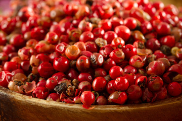 red peppercorn seeds in wooden plate