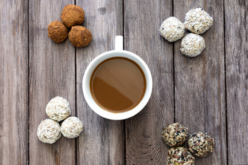 Healthy breakfast concept, four types of protein balls or energy bars on a wooden background in the center a white cup of coffee, horizontal orientation