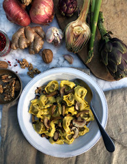 Stuffed ravioli pasta with fried mushrooms and walnuts, styled with brown vegetables on the marble table