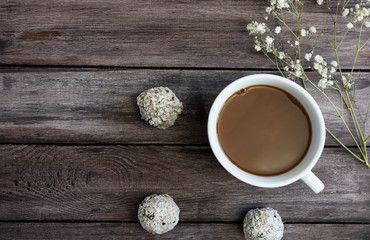 Obraz na płótnie Canvas energy balls with a cup of coffee and white flowers on a wooden background, the concept of a healthy breakfast, copy space, healthy sweets, sweets from oatmeal, raisins in coconut flakes