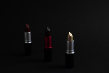 Three lipsticks on a dark background, low key photo, natural decorative cosmetics, horizontal orientation