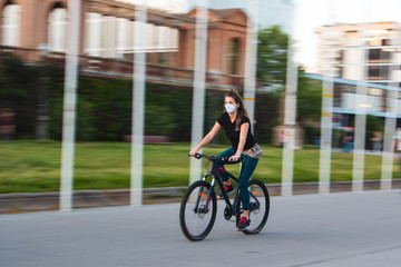 Chica joven de ojos claros, yendo en bicicleta durante coronavirus en una ciudad.