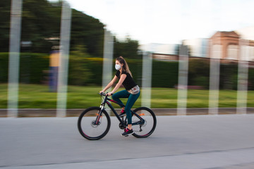 Chica joven de ojos claros, yendo en bicicleta durante coronavirus en una ciudad.