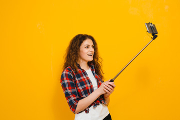Beautiful brunette girl who makes her selfie and smiles on a yellow background