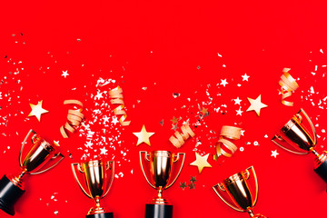 Three golden winner cups with confetti on a red background. Flat lay style. Competitions concept.
