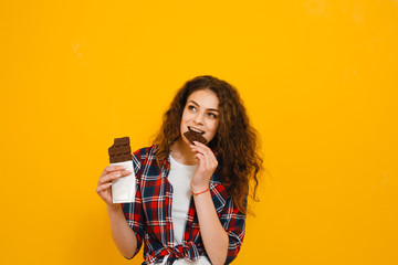 Brunette girl with chocolate in her hand that smells its taste over a  yellow background