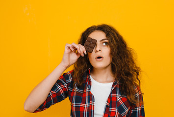 Brunette girl with chocolate in her hand that smells its taste over a  yellow background