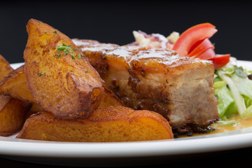 Pork ribs with roasted potatoes, cabbage and lettuce in a white ceramic plate on a wooden table