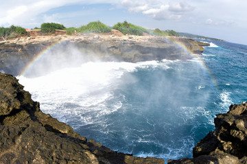 There's a rainbow over the sea looking down from the cliffs. Devils tears on rembongan island