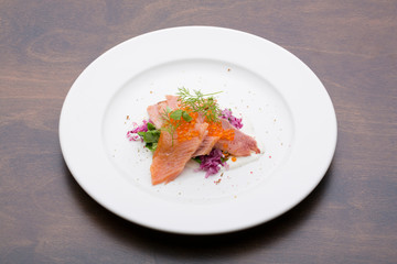 Salmon with caviar on a white ceramic plate on a wooden table