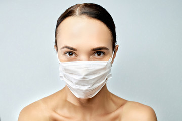 Young brunette girl with beautiful eyebrows and brown eyes looks with a grin on her face a white medical mask  on a gray background