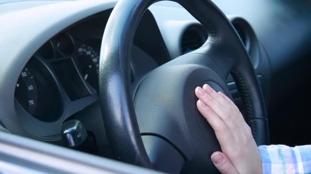 The hand of a woman presses on the steering wheel of a car. Nervous unrecognized driver beeping in car. Technology and transportation concepts.