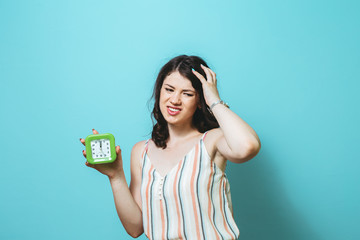 Image of a sad thinking young Asian  woman posing isolated over pink wall background holding clock.