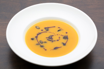Yellow pumpkin soup in a white ceramic plate on a wooden table