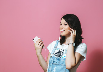 Image of happy Asian woman wearing earphones singing and dancing isolated over pink background