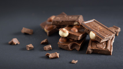 Milk chocolate pieces stack with hazelnut and crumbs on a black background. Closeup stacked bars of chocolate and nuts