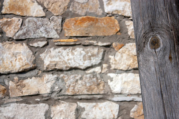 Cracked vertical log close-up on a blurred background of masonry. Texture and cracks of a wooden log close-up. Fragment of a wall of stones of different sizes, as a blurred background.