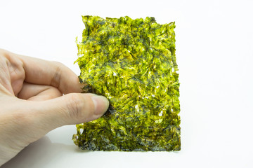 Close-up view of the hand holding a piece of roasted seaweed sheet isolated on white background. © gracethang