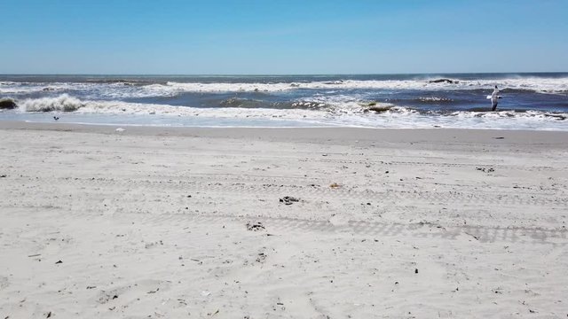 Low view of the ocean with small waves from a smooth windy beach with sand blowing 