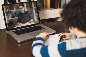 Young student engaged in a distance learning class with his teacher via video conference on a laptop, studying from home.