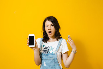 Naklejka premium Portrait of a shocked young asian woman showing blank screen mobile phone isolated over yellow background