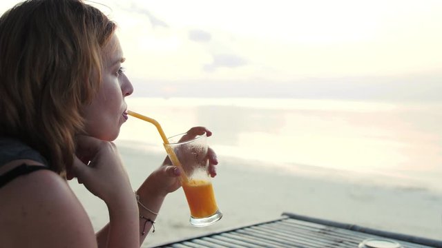 Young woman drinking cocktail on the beach at sunset on background.