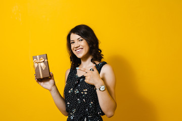 Portrait of a young  beautiful asian girl holding a gift and happy over a yellow background