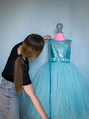 a seamstress is measuring a blue dress for a little girl