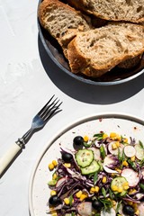 Photo of a fresh spring salad on a white porcelain plate and vegetable mix of ingredients in metal bowl on a white rustic background sunlight with shadows

