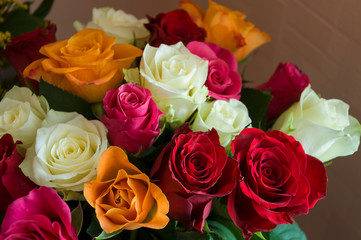 Lovely big colorful bouquet with many flowers  roses of red, vinous, orange and white colors. Green leaves and thorns. Still life. Calm pink background