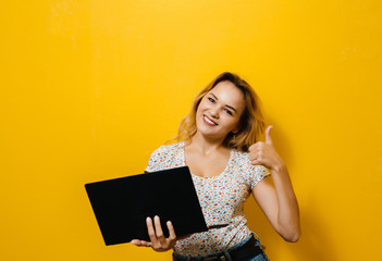 Image of a young girl holding a laptop and with winner  gesture hand over yellow background