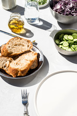 Photo of a fresh spring salad on a white porcelain plate and vegetable mix of ingredients in metal bowl on a white rustic background sunlight with shadows
