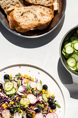 Photo of a fresh spring salad on a white porcelain plate and vegetable mix of ingredients in metal bowl on a white rustic background sunlight with shadows
