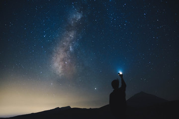 Blurred silhouette of a man observing the starry sky with the milky way and a flashlight in his hand