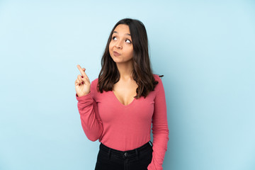 Fototapeta premium Young mixed race woman isolated on blue background with fingers crossing and wishing the best