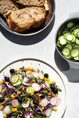 Photo of a fresh spring salad on a white porcelain plate and vegetable mix of ingredients in metal bowl on a white rustic background sunlight with shadows
