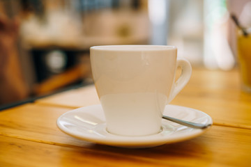White cup with coffee on a plate. Hot espresso in a cup on a wooden table. Espresso for breakfast in a cafe