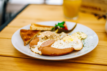 Helpful appetizing breakfast on a white plate. Scrambled eggs with vegetables and croutons in a cafe. Breakfast in the cafe: scrambled eggs, sausages and toast