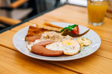 Helpful appetizing breakfast on a white plate. Scrambled eggs with vegetables and croutons in a cafe. Breakfast in the cafe: scrambled eggs, sausages and toast