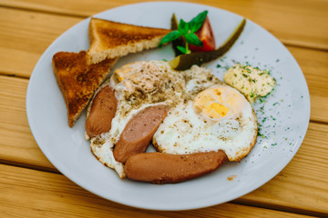 Fried eggs with tomatoes, cucumbers and cheese for breakfast. Scrambled eggs with sausages and tomatoes in a cafe. Comprehensive breakfast with eggs, ham, vegetables and toast